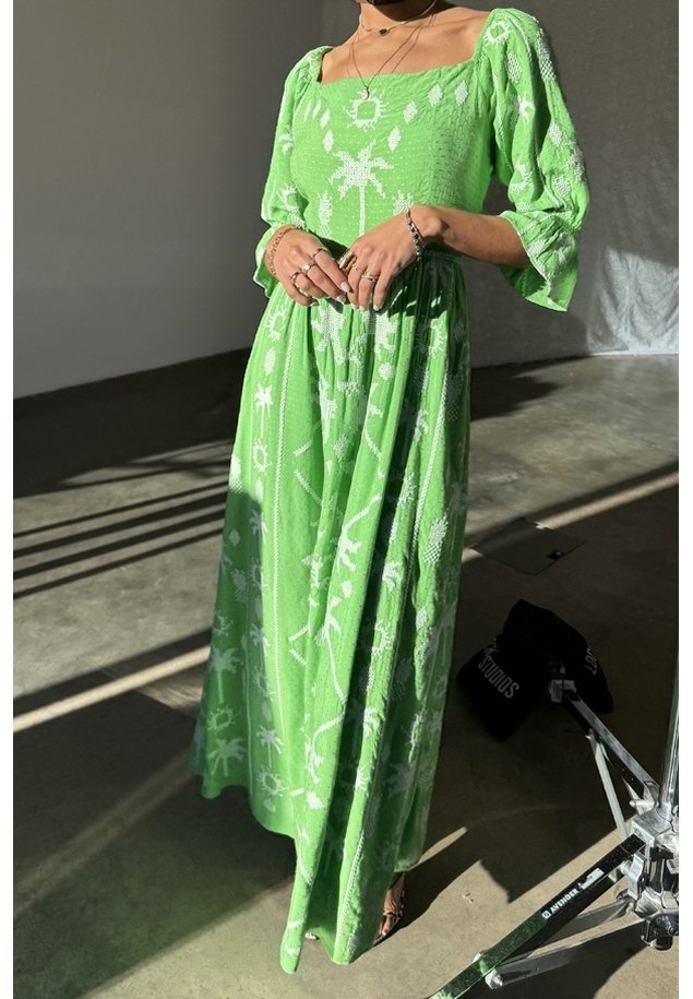 Lång, grön klänning med fyrkantig halsringning och puffärm. Har vita blommor och solmönster. Tillverkad av texturerad tyg.