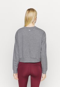 Sweatshirt gris court à manches longues, col rond, avec un discret logo CK au dos, associé à des leggings bordeaux. Texture lisse.
