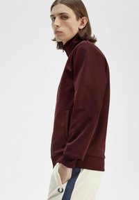 Giacca zip-up color bordeaux realizzata in un tessuto liscio, con colletto alto, tasche laterali e polsini e orlo a coste.