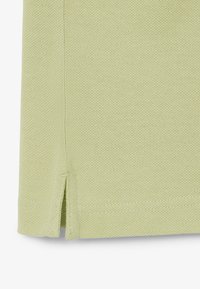 Hellgrüner, strukturierter Stoff mit einem Seitenschlitz und sichtbarer Naht am Saum eines Kleidungsstücks.