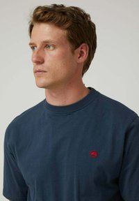 Camiseta de algodón de manga corta en azul marino con un pequeño logo rojo en el lado izquierdo del pecho y un clásico cuello redondo. Textura suave.