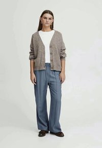 Cardigã de malha bege com botões, combinado com calças largas azul claro e uma t-shirt branca. Textura suave e ajuste casual.
