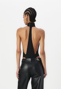 Czarny bodysuit na halter z głębokim dekoltem na plecach, wykonany z miękkiego materiału. Połączony z czarnymi spodniami z wysokim stanem wykonanymi z ekologicznej skóry, z metką z logo.