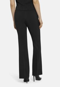 Zwarte flared broeken met een gladde textuur, gemaakt van geweven stof. Voorzien van een aansluitende taille en achterzakken, gecombineerd met hoge hakken.