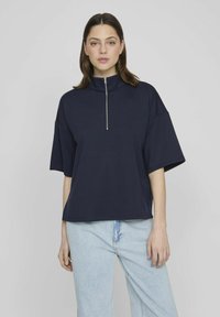 Suéter azul marino con cuello alto y mangas cortas, que cuenta con un cierre de cremallera en el cuello. Fabricado en tela suave con un ajuste relajado.