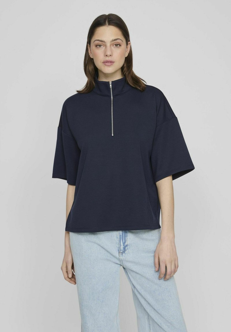 Suéter azul marino con cuello alto y mangas cortas, que cuenta con un cierre de cremallera en el cuello. Fabricado en tela suave con un ajuste relajado.