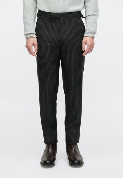 Tamne hlače na prugice od tkanog materijala s krojem po mjeri, s remenom u struku i uparene s tamnim gležnjačama.