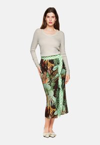 Helle beige, enganliegende Pullover mit langen Ärmeln, kombiniert mit einem gemusterten, knielangen Rock in Grün-, Braun- und Blumendesigns.