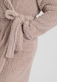 Lys pink, fluffy badekåbe med en bundet bælte og lommer, der har et tekstureret stof og lange ærmer for komfort og varme.