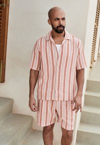 Camisa de manga corta con cuello y botones, y pantalones cortos a juego en color coral con rayas verticales blancas y patrón texturizado.