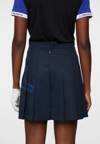 Mörkblå plisserad kjol med en slät yta och blå logodetalj på framsidan, utrustad med en dold dragkedja bak och skräddarsydd passform.
