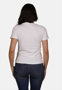 T-shirt bianco in cotone aderente con maniche corte, colletto rotondo e superficie liscia, abbinato a jeans in denim blu con tasche posteriori.