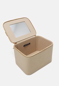 Beige storage box with gold zipper, square shape, and an interior mirror. Brand label visible inside. Soft texture, minimalistic design.