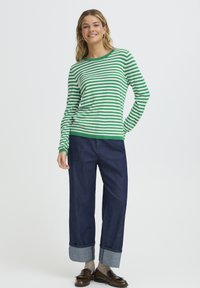 Chemise à manches longues rayée vert et blanc associée à un jean large bleu foncé avec ourlets retroussés et mocassins marron.