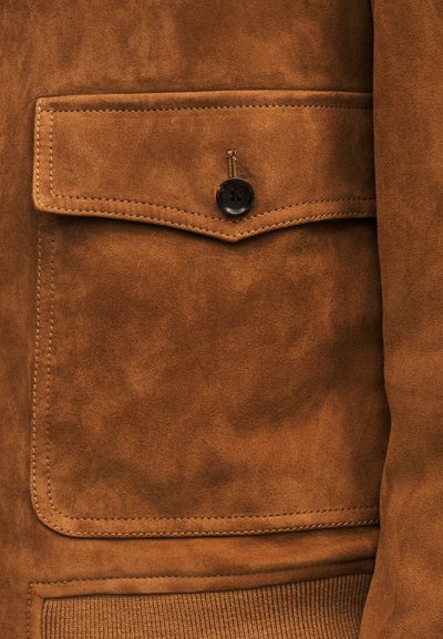 Brown suede jacket pocket with a flap secured by a single dark button and detailed stitching on the edges.