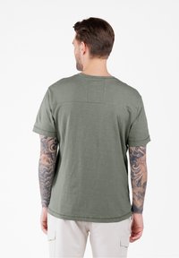 Olijfgroene T-shirt met korte mouwen, een relaxte pasvorm, een ronde hals en een rechthoekige patch op de bovenrug. Zachte textuur, casual ontwerp.