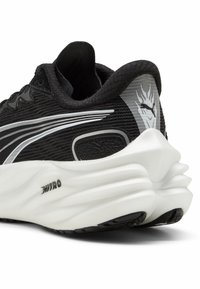 Chaussure de sport noire avec upper texturé, semelle intermédiaire blanche, design incurvé, logo de marque bien visible au niveau du talon et accents réfléchissants.