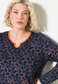 Mörkblå skjorta med ett stjärnmönster i orange, med V-ringning och lång ärm. Tillverkad av mjukt tyg med en slät yta.