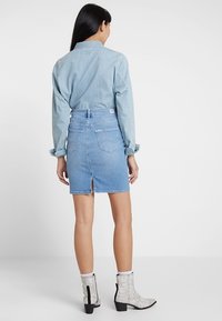 Ljusblå denimkjol med en slits bak, i kombination med en ljus chambrayskjorta. Den har två bakfickor och en hög midja.