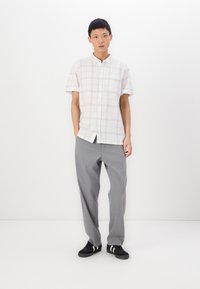 Chemise à manches courtes, col classique en crème clair avec un motif à carreaux noirs, assortie à un pantalon gris ample et des baskets noires avec des rayures blanches.