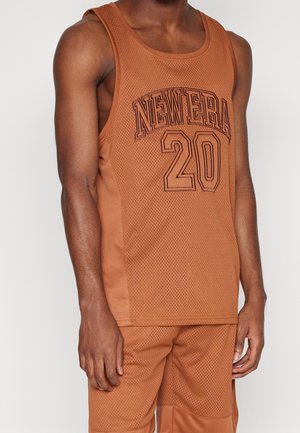 Man wearing brown mesh tank top and matching shorts, tank top features "NEW ERA 20" text in large outlined letters.