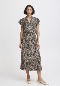 Robe à imprimé léopard avec col, manches courtes à volants et jupe fluide. Tissu doux dans des tons beige et marron. Portée avec des chaussures couleur crème.