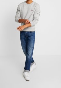 Grijze trui met ronde hals, geribbelde manchetten en logo detail. Gecombineerd met blauwe spijkerbroek en witte sneakers. Casual pasvorm en eenvoudig ontwerp.