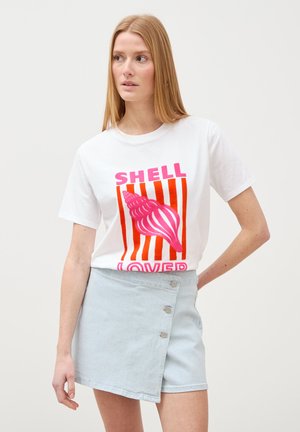Frau trägt weißes T-Shirt mit pinker Muschelgrafik und dem Schriftzug „Shell Lover“, kombiniert mit einem hellblauen Rock mit Knöpfen.