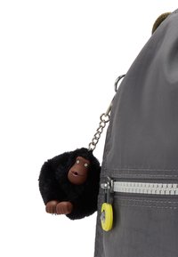 Grijze stoffen rugzak met een gestructureerd oppervlak en een kleine, zwarte, fuzzy gorilla sleutelhanger met een bruine gezicht, bevestigd met een ketting.