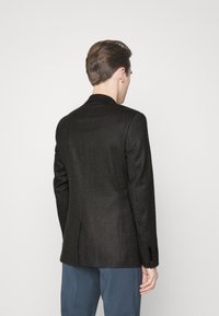 Ciemnoszara marynarka o dopasowanym kroju z teksturowanej tkaniny, z klapkami i zapięciem na trzy guziki; posiada dwa tylne rozcięcia oraz kontrastowe guziki.