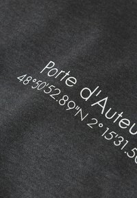 Sort stof med hvid tekst. Teksten lyder "Porte d'Auteuil 48°50'52.89"N 2°15'31.56". Blød tekstur, afslappet design.