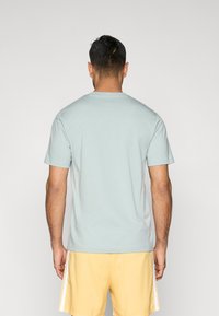 helehall sinine puuvillane T-s�ärk ümmarguse kaelusega ja lühikeste varrukatega, kantud kollaste lühikeste pükstega. Ühtlane tekstuur, nähtavaid mustreid ega aktsente pole.