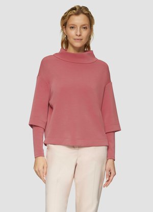 Pullover rosa, oversize, con colletto a cowl e maniche ampie. Tessuto morbido con una vestibilità comoda, abbinato a pantaloni di colore chiaro.