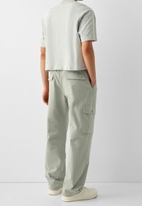 Hellgraues, kurzes T-Shirt kombiniert mit locker sitzenden, hellgrünen Cargohosen. Die Hosen verfügen über Seitentaschen und eine entspannte Silhouette.