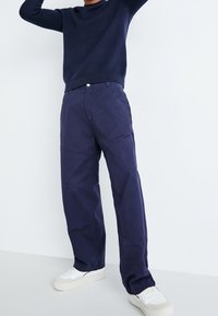 Marinblå bomullsblandade byxor med raka ben, med en knappstängning och fickor. Bärs med vita sneakers.