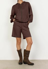 Bruine zip-up hoodie met voorzakken, gecombineerd met bijpassende bruine短en. Kniehoge bruine laarzen met een licht gestructureerd oppervlak.