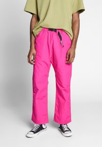 Ljusrosa byxor med lös passform, tillverkade av lätt material, med resårmidja och ett svart justerbart bälte.