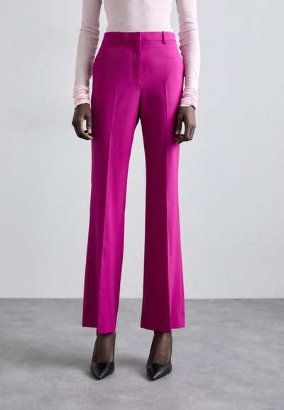 Pantalons fuchsia ajustés avec une coupe slim, taille haute et jambes larges. Texture lisse, détails de plis à l'avant, associés à des talons aiguilles noirs.