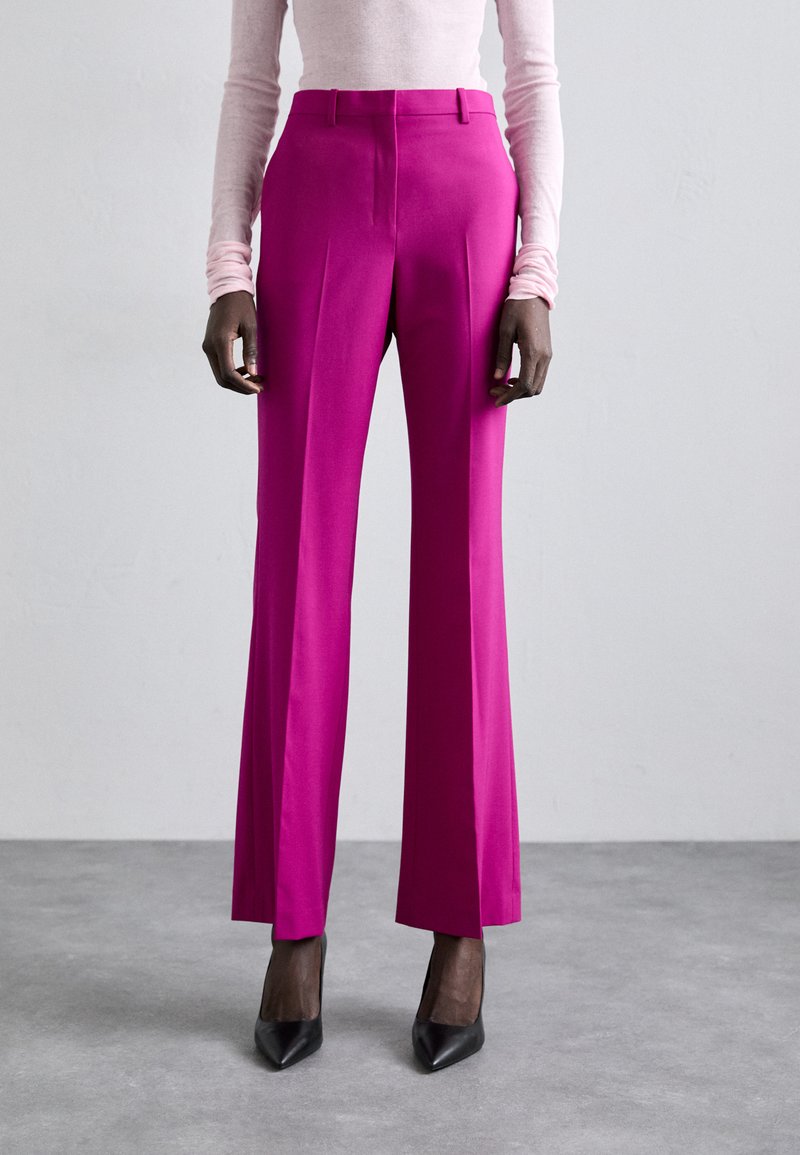 Fuksiat räätälöidyt housut, joissa on slim fit, korkea vyötärö ja leveät lahkeet. Sileäpintainen rakenne, taitteet edessä, yhdistetty mustiin teräväkärkisiin korkokenkiin.