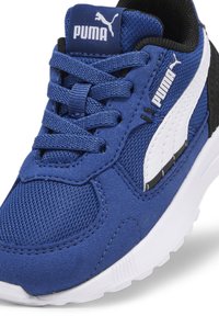 Sininen kangaslenkkari mustilla ja valkoisilla yksityiskohdilla; siinä on tekstiilimateriaali, pyöreä kärki ja nauhakiinnitys. Puma-logo näkyy kielekkeessä.