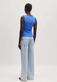 Blauwe mouwloze top gecombineerd met lichtblauwe wijde jeans. Bevat een ronde halslijn en achterzakken op de jeans. Effen kleuren, geen patronen.
