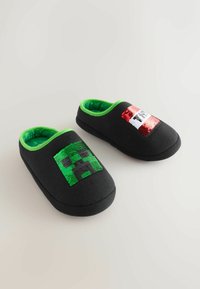 Black fabric slippers with green lining, featuring sequin designs: one with a green pixelated face and the other with a red and white striped pattern.
