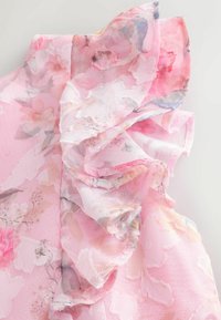 Rosa Bluse mit Blumenmuster aus transparenter Stoff mit gestuften Rüschen. Das Design umfasst leichte Blumenmuster in sanften Farbtönen und zarten Kanten.