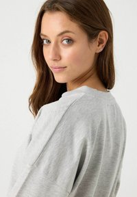 Sudadera gris con un corte relajado, cuello redondo y costuras de hombro caído. Textura de tela suave, diseño minimalista y sin patrones visibles.