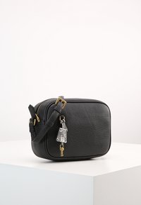 Black leather crossbody bag with a textured finish, rectangular shape, gold hardware, and a key charm hanging from the zipper.