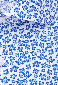 Biała tkanina z wzorem małych i średnich niebieskich kwiatów hibiskusa, pokazująca guzik i część kołnierzyka.