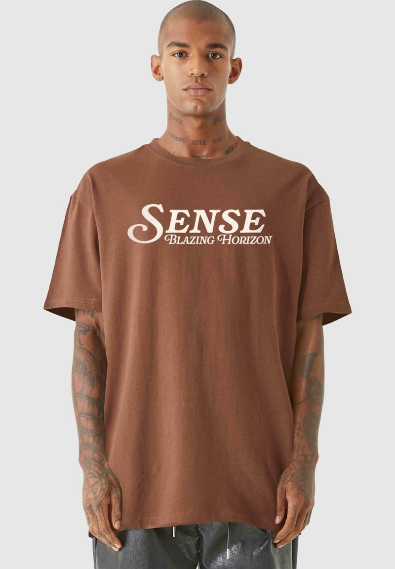Hnedé bavlnené tričko s prednou grafikou v bielej farbe s nápisom "SENSE BLAZING HORIZON", uvoľneného strihu a krátkymi rukávmi.