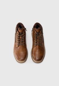 Braune Leder-Stiefeletten mit strukturiertem Finish, Schnürdesign, seitlichen Reißverschlüssen und weichem Fellfutter. Helle, tanfarbene Sohle und Schnürsenkel.
