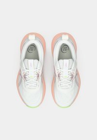 White athletic sneakers feature a mesh upper, pink rubber sole, green accents, and a lace-up design with a padded tongue.