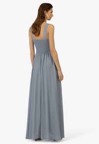Lichtblauwe maxi-jurk met smock achterzijde, brede bandjes en een vloeiende rok van doorschijnende chiffonstof. Subtiele textuur, lichtgewicht ontwerp.